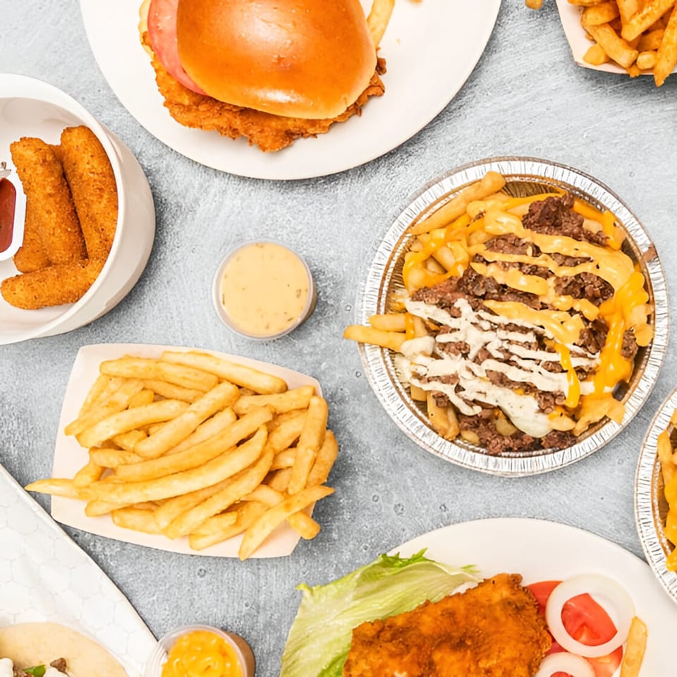 An overhead view of Kebabish Grill's fried chicken sandwiches, loaded fries, mozzarella sticks, and sauces.