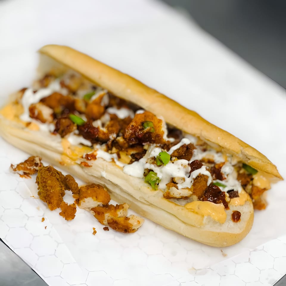 A Kebabish Grill & Fried Chicken sub sandwich filled with fried chicken, white sauce, and green onions.