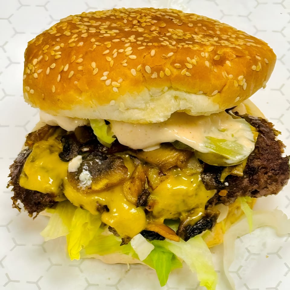 A Kebabish Grill & Fried Chicken halal burger with melted cheese, lettuce, pickles, and sauce.